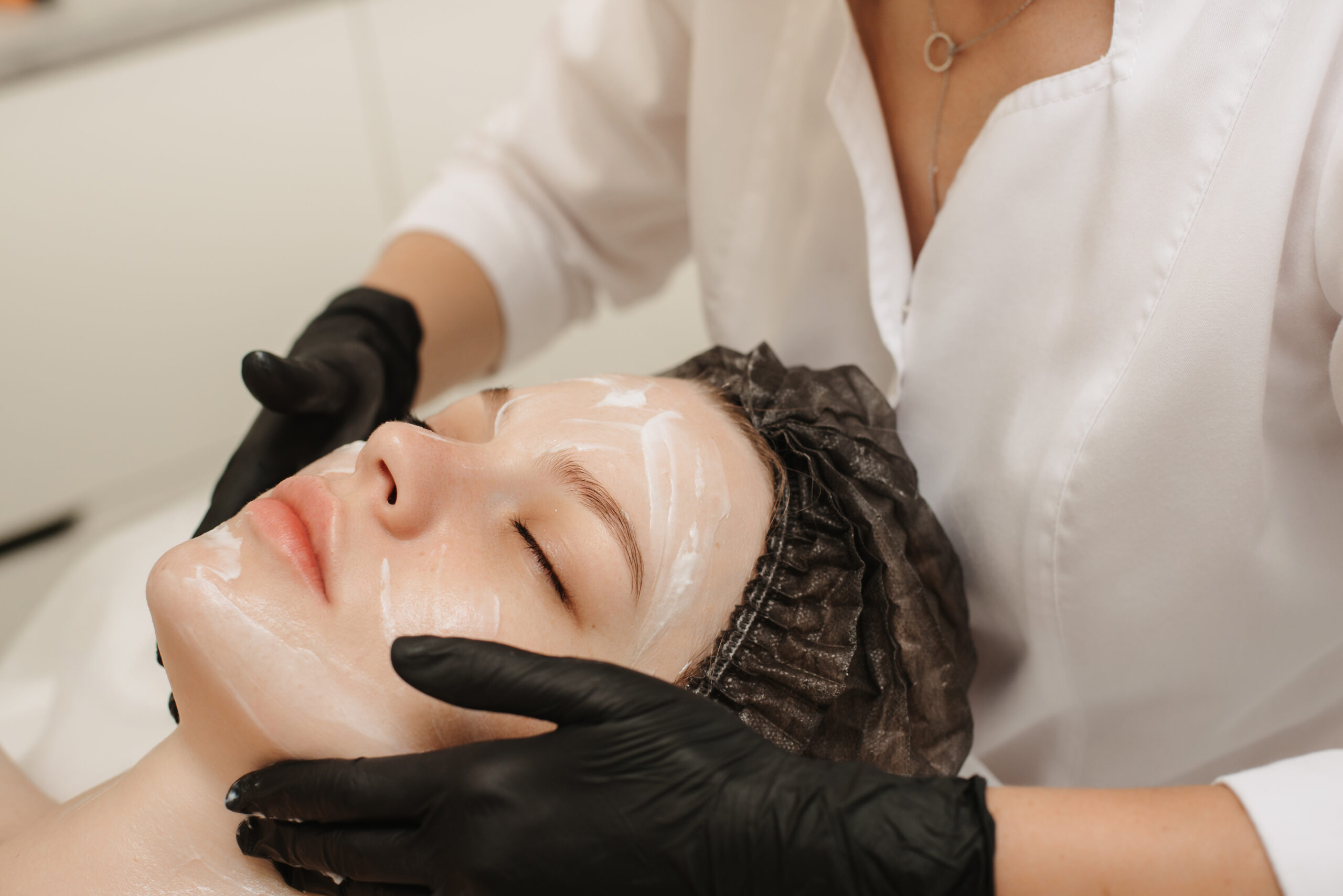 Close-up of the beautician’s hands applying cream to the client’s face and doing a massage. Facial skin care. Spa therapy in Cave Creek, AZ: Just Breathe by Jodi offers relaxing facials for wellness and stress relief in a serene setting.